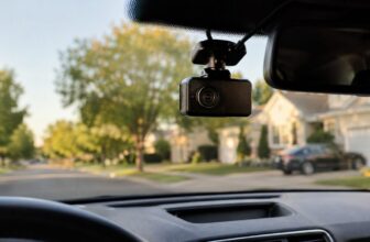 Black dash cam mounted on a car windshield with a suburban street ahead